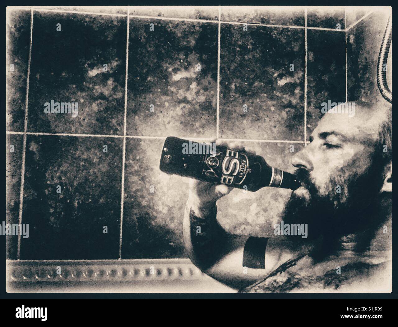 Bearded tattooed man drinking real ale from the bottle in a hot bath. Stock Photo