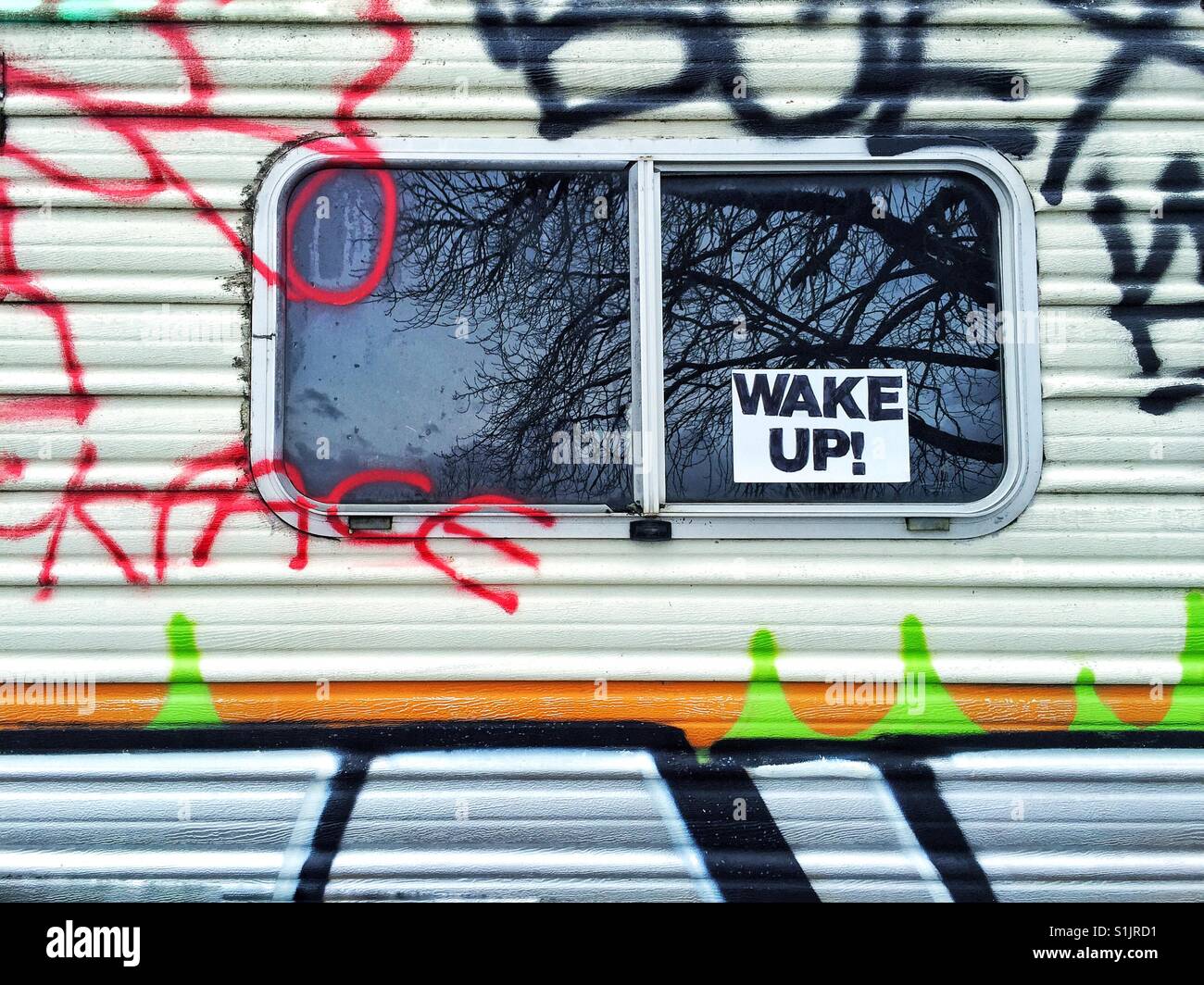 Window of a graffiti covered motorhome with sign Wake Up Stock Photo