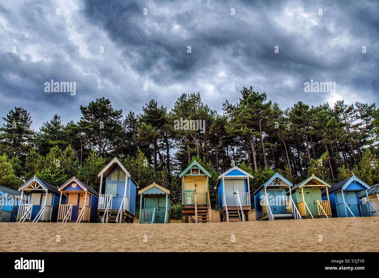 Rows of colourful beach huts on a deserted beach with storm clouds and stormy skies above. - Smartphone Captured Stock Image