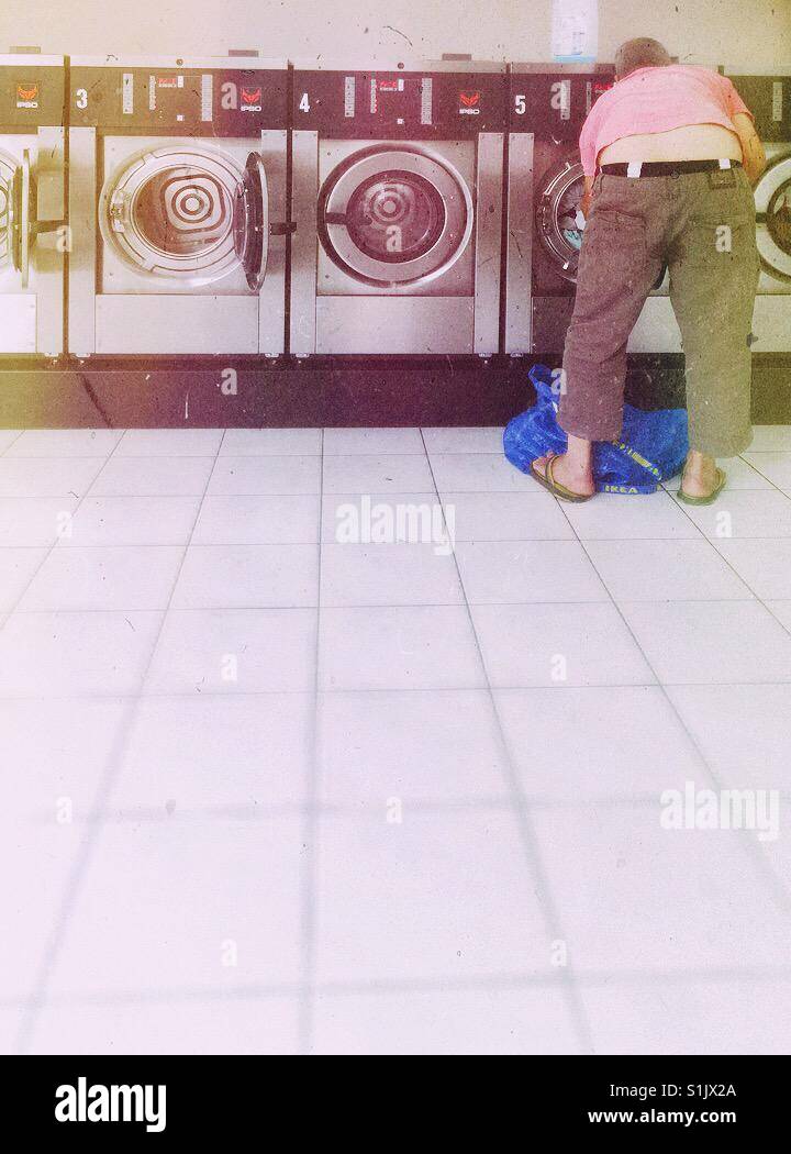Laundry day. Man in slippers wearing a pink t-shirt preparing his laundry. - Smartphone Captured Stock Image