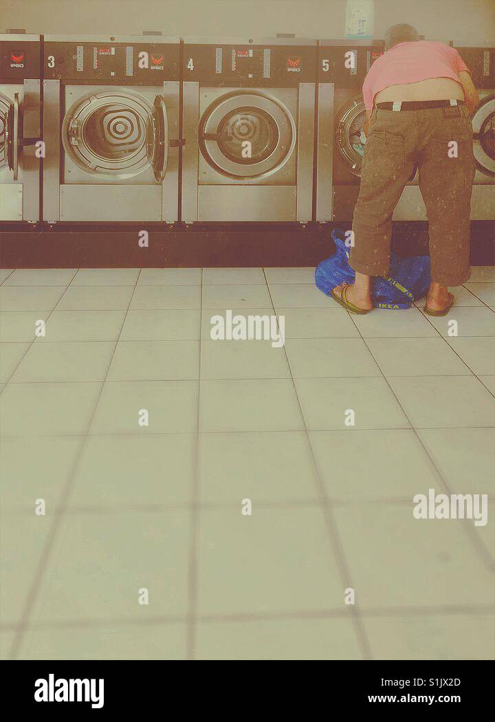 Laundry day. Man with slippers and pink t-shirt preparing his laundry. - Smartphone Captured Stock Image