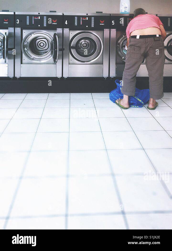 Laundry day. Man wearing slippers and a pink t-shirt preparing his laundry. - Smartphone Captured Stock Image