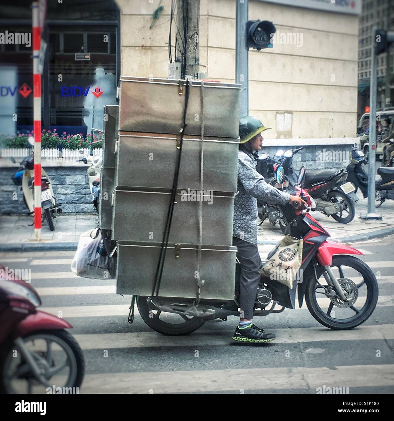 Vietnamese man on moped carrying an oversize load of metal boxes on a city street Stock Photo