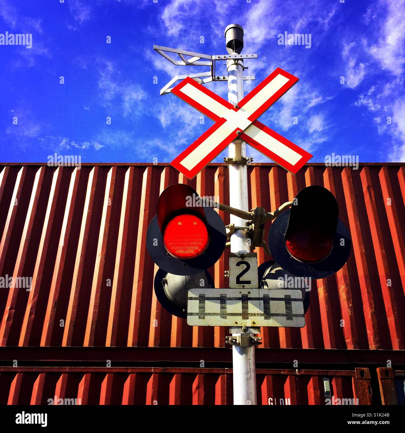 Lights flashing at a railway crossing while a cargo train passes Stock Photo
