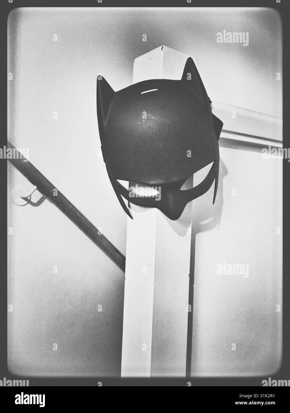 Batman mask hanging from a staircase bannister. Stock Photo