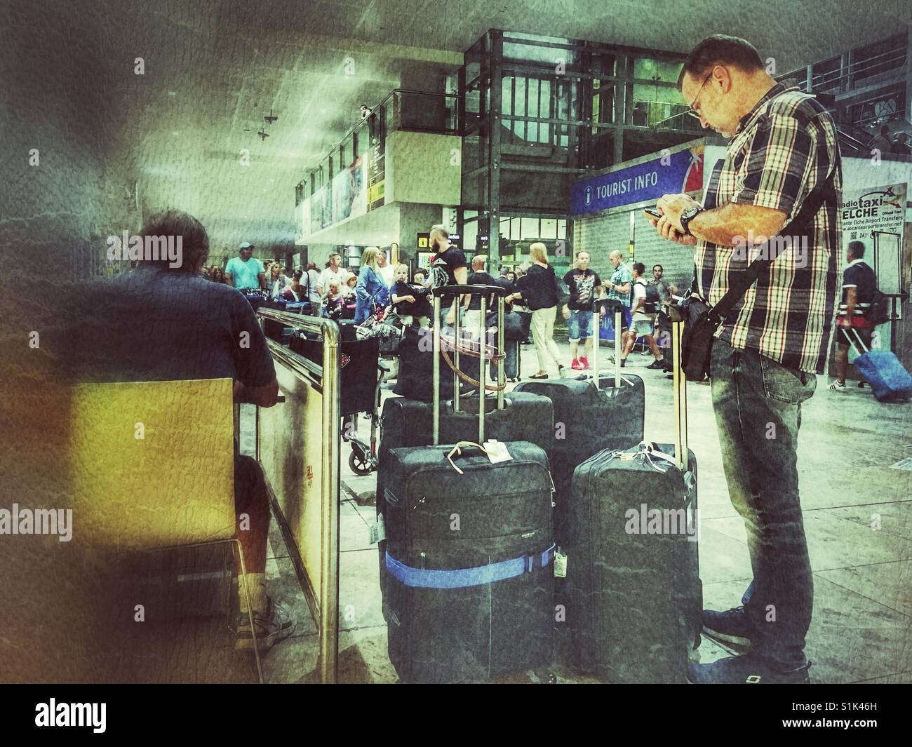 Man standing with lots of luggage and using mobile phone in the arrivals area of El Altet airport, Alicante, Spain - Smartphone Captured Stock Image Man standing with lots of luggage and using mobile phone in the arrivals area of El Altet airport, Alicante, Spain - Smartphone Captured Stock Image