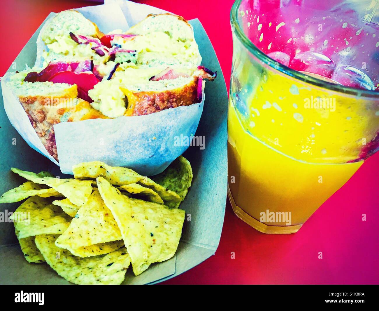 Scrambled egg and bacon in a bagel with tortilla chips and a glass of orange juice. - Smartphone Captured Stock Image