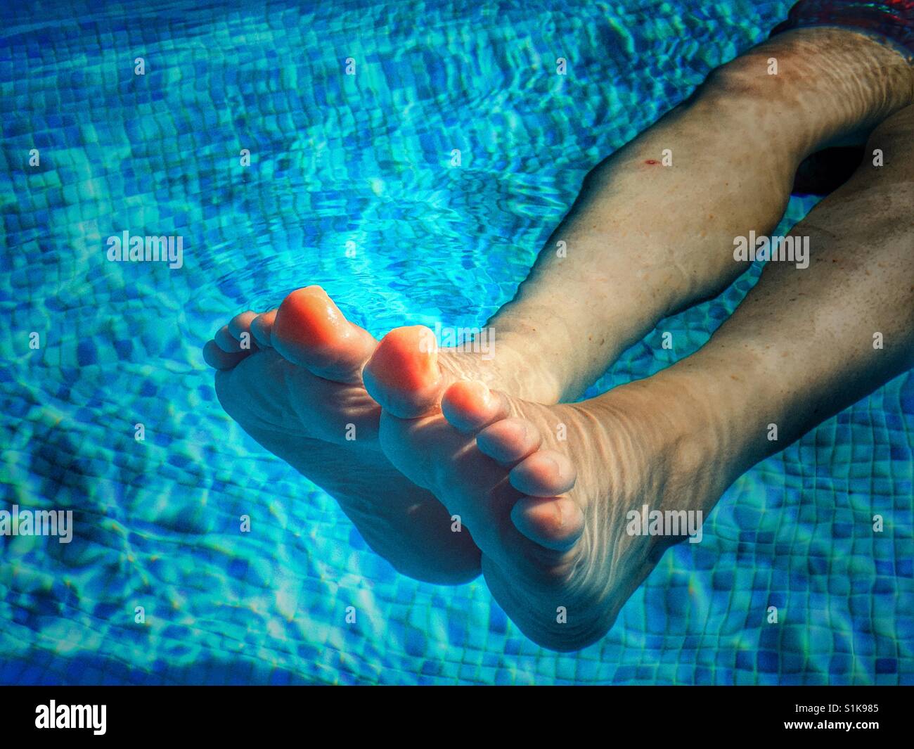 Woman floating in swimming pool, focus on legs and feet Stock Photo