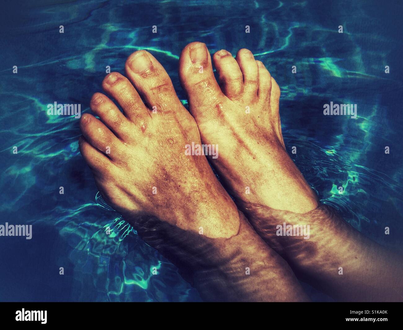Keeping cool. Feet in a swimming pool - Smartphone Captured Stock Image