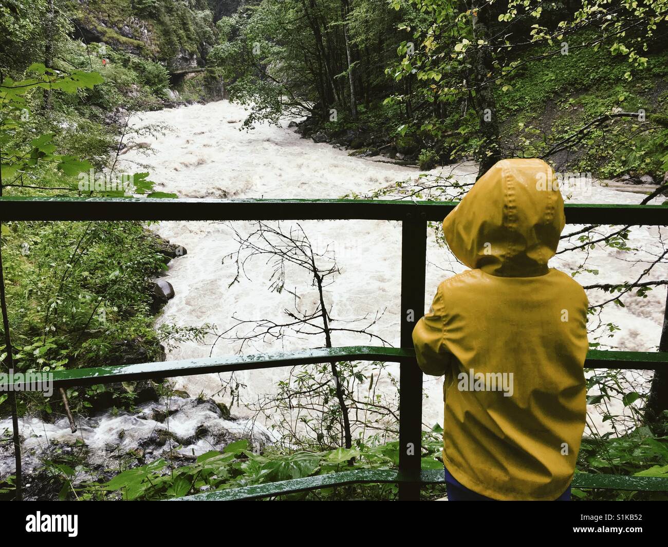 Young boy in yellow raincoat looking at wild mountain river Stock Photo