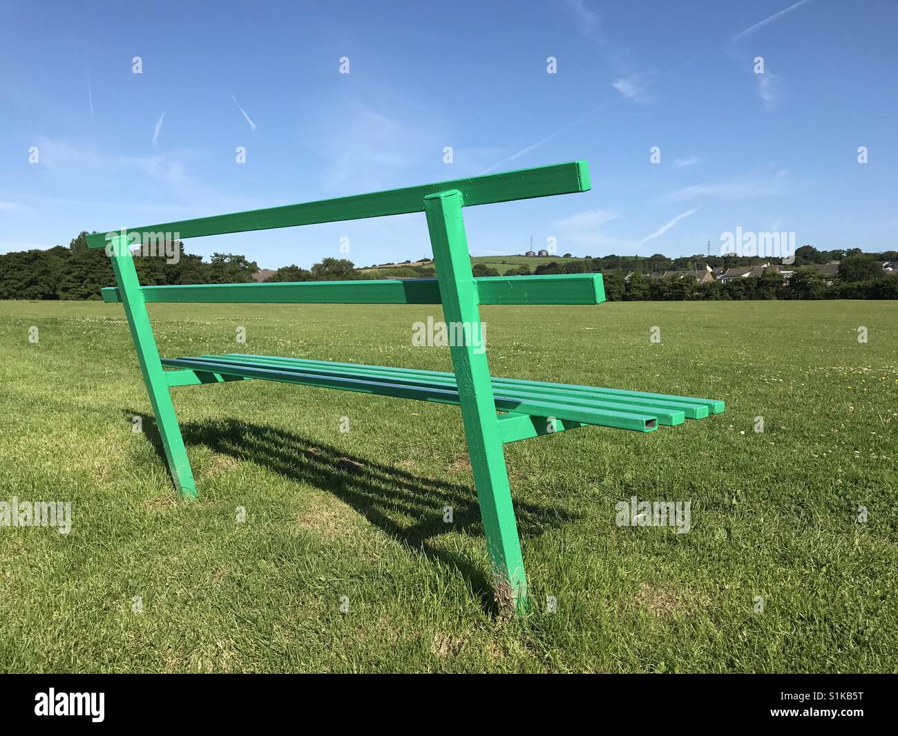 Empty green bench in a public park with a cricket pitch (landscape format) Stock Photo