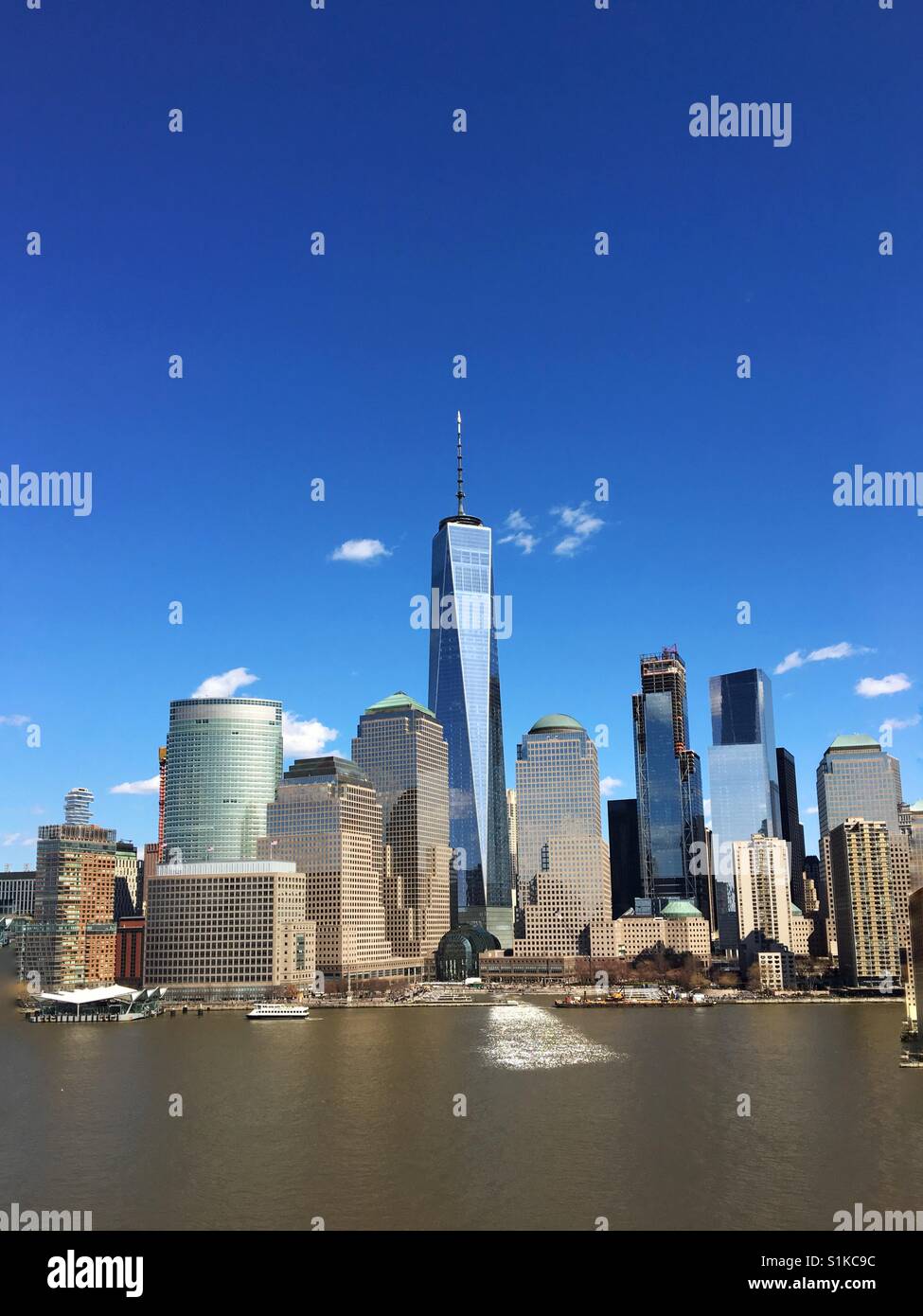 The skyline of lower Manhattan featuring a famous landmark, which is reflected in the calm waters of the Hudson River - Smartphone Captured Stock Image