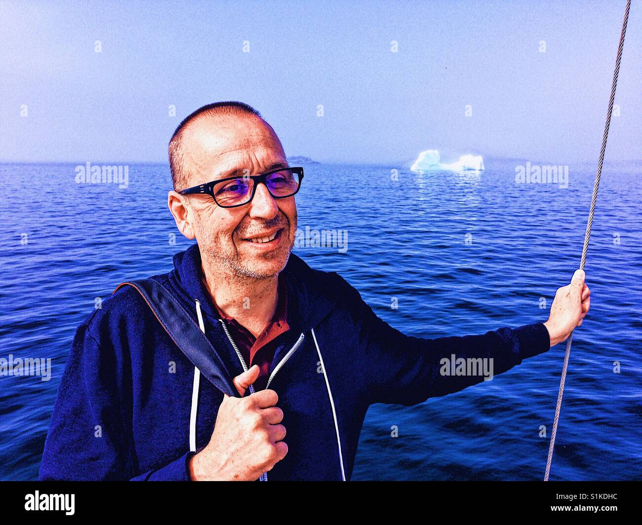Smiling middle aged man and iceberg in summer, Northern Peninsula, Newfoundland, Canada - Smartphone Captured Stock Image