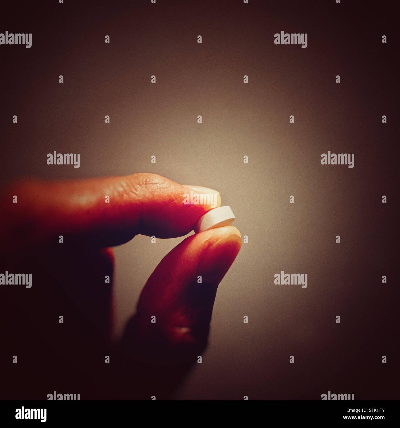 A man holding a round white tablet between thumb and index finger - Smartphone Captured Stock Image