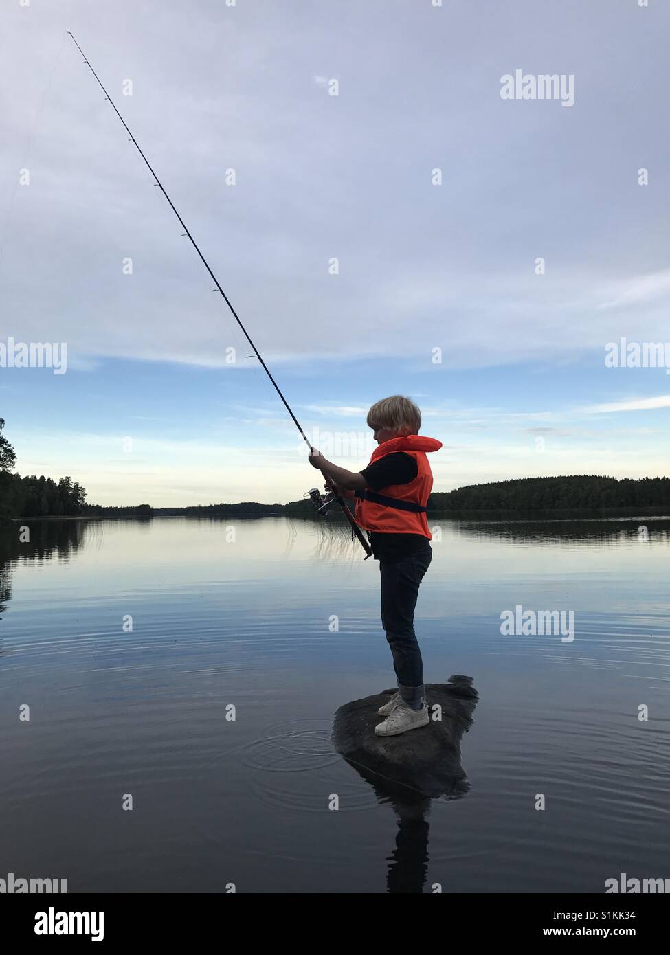 Skyline fishing Island life jacket fishing rod lake sky magic still Water summer boy athmosphere Stock Photo