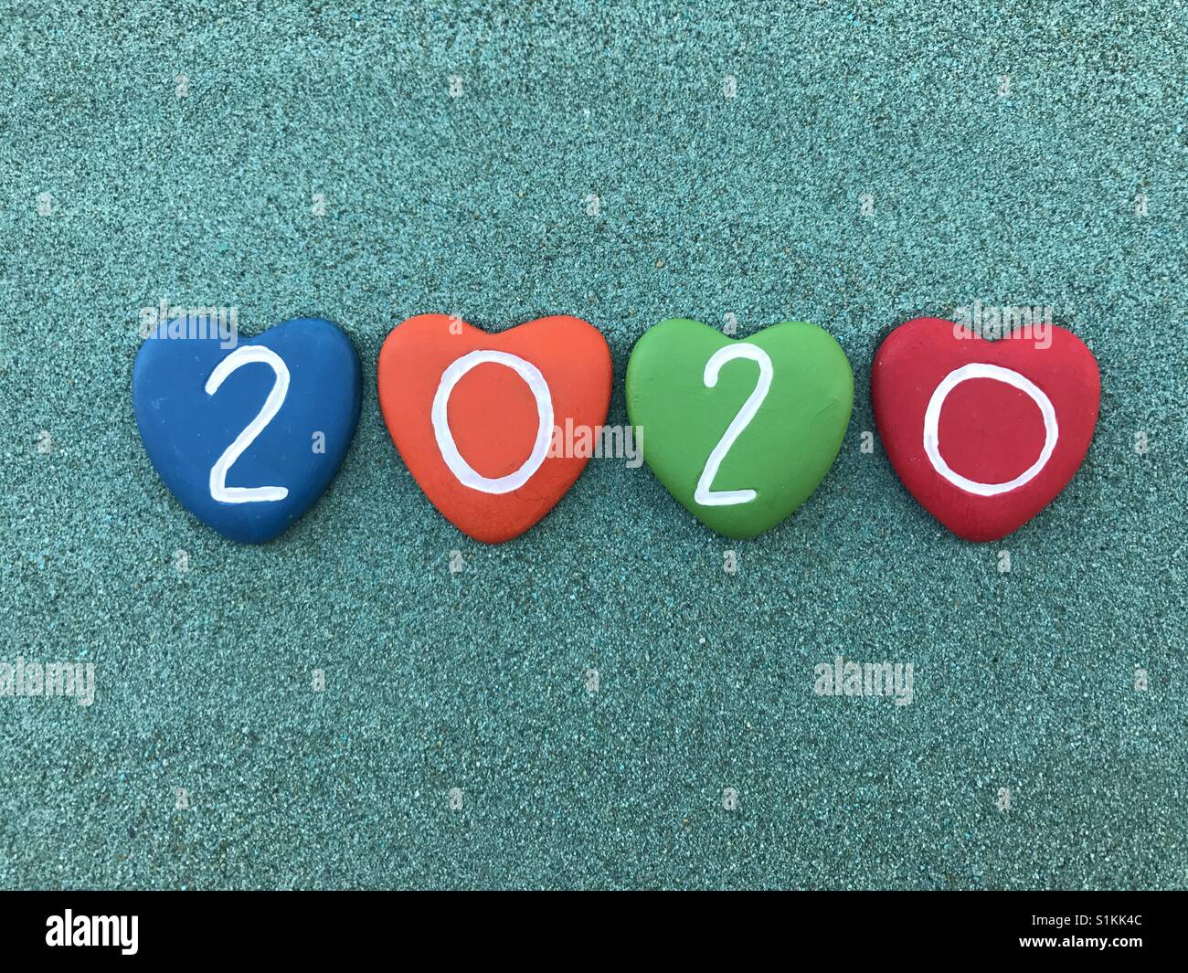 Year 2020 carved and painted on heart stones over green sand Stock Photo