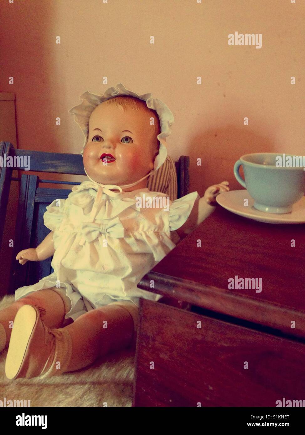 Doris takes her tea- beloved babydoll posed for tea party wearing dress and bonnet in blue chair - Smartphone Captured Stock Image