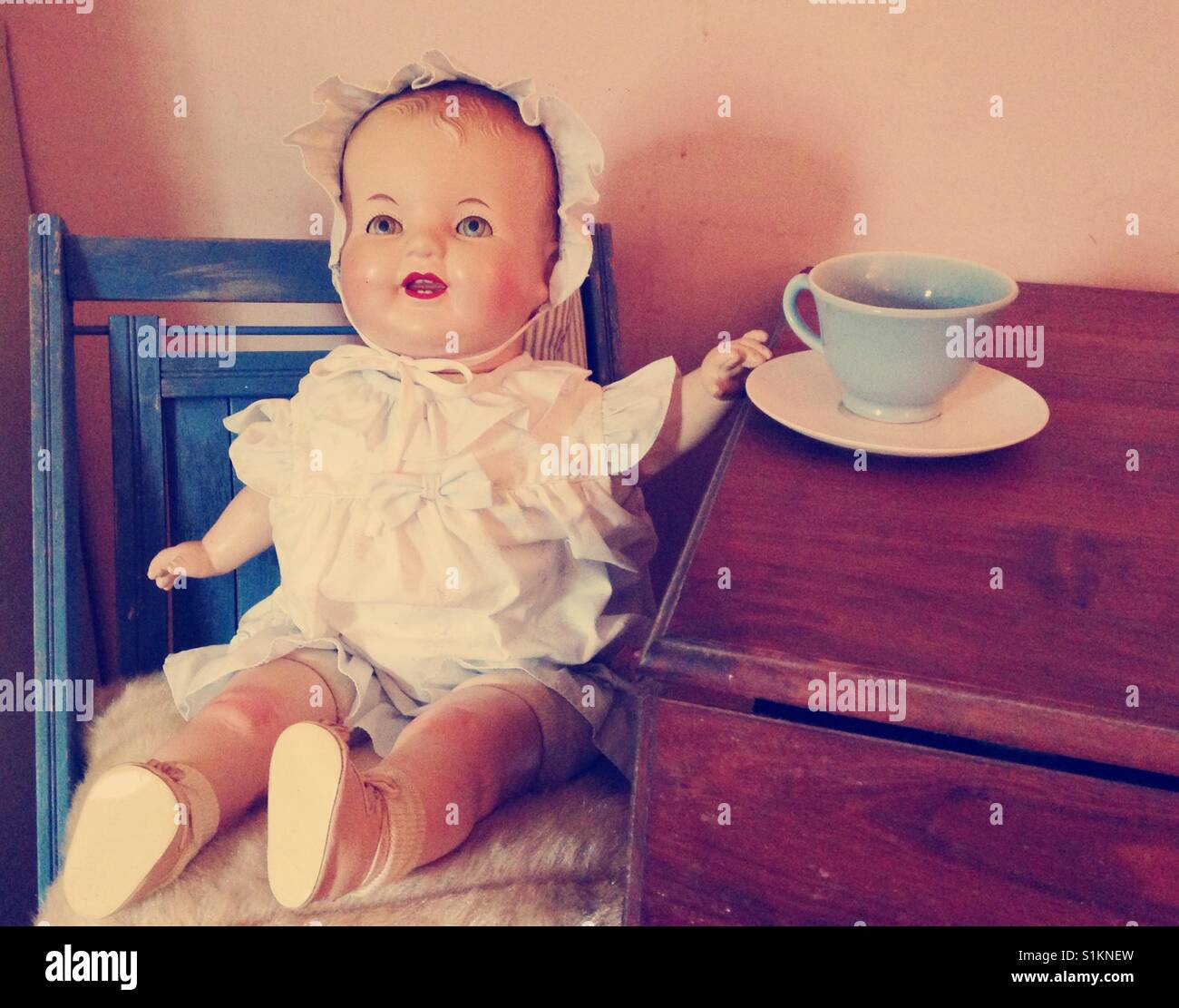 More tea, please- Doris the doll awaits tea while sitting in blue chair and wearing blue and white dress and ruffled bonnet - Smartphone Captured Stock Image