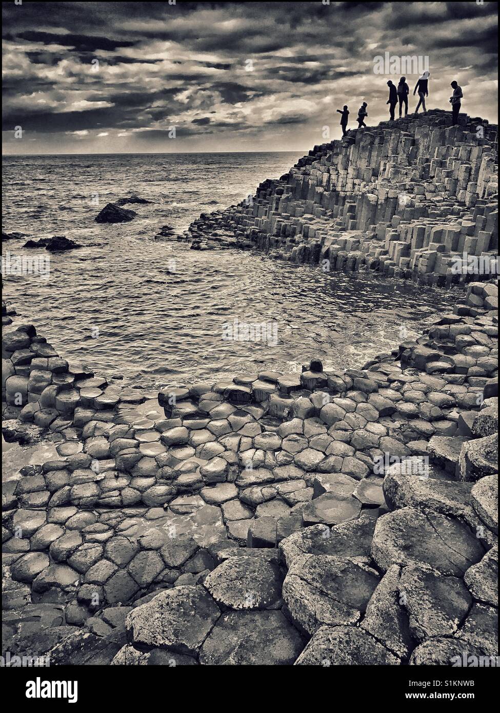 An atmospheric image of tourists walking over the volcanic basalt rock columns at Giant's Causeway in Northern Ireland. This natural phenomenon is a UNESCO World Heritage Site. Photo © COLIN HOSKINS. - Smartphone Captured Stock Image