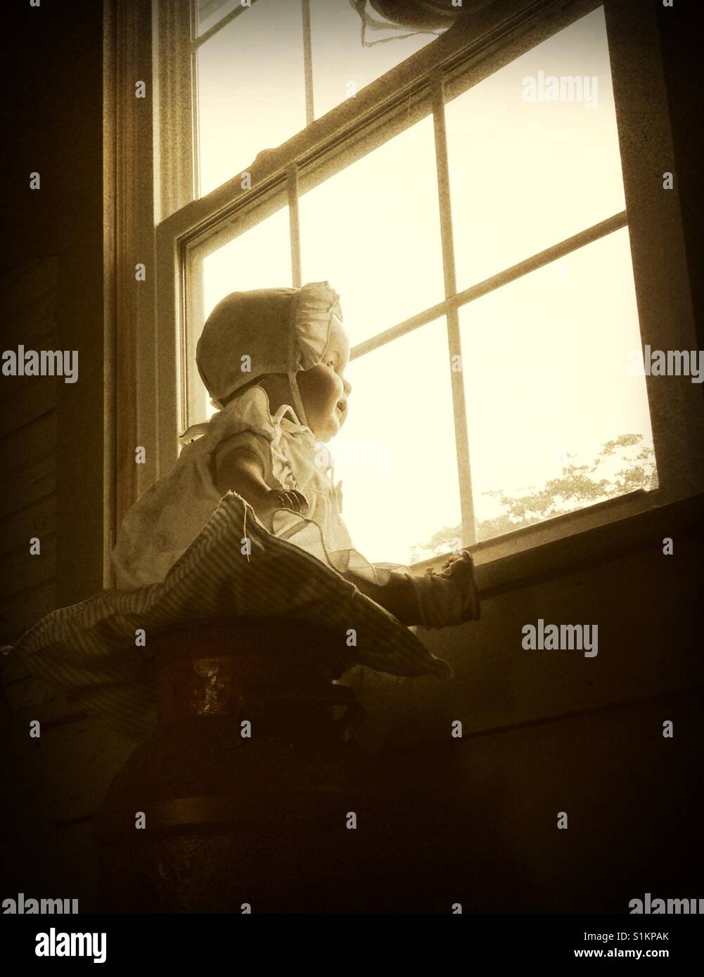 The wait- Doris the composition doll scans out window of old house dressed in bonnet, dress, socks and shoes Stock Photo