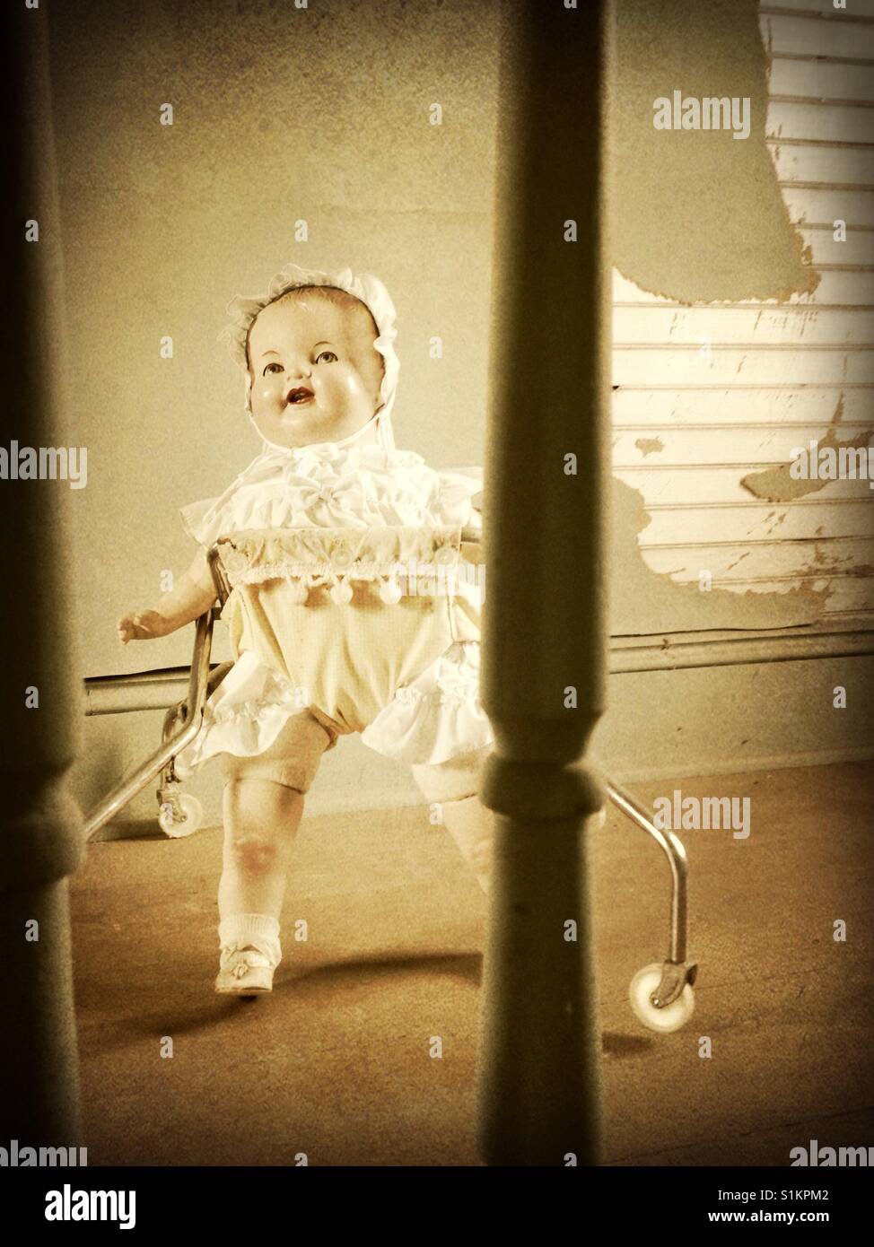 Watching Doris walk- old composition doll with ruffled bonnet and dress in vintage gingham baby walker inside old house with wooden floors, railing, bead board and green wallpaper Stock Photo
