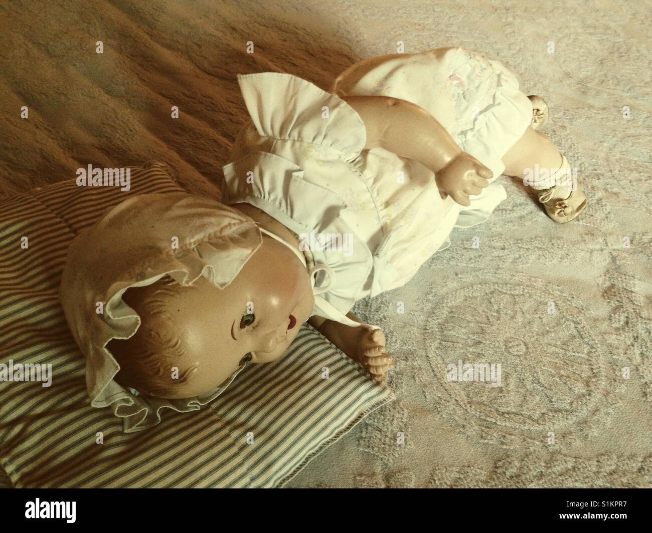 Doris can roll over- composition doll on bed wearing ruffles bonnet and dress, shoes and socks, with blue ticking pillow - Smartphone Captured Stock Image