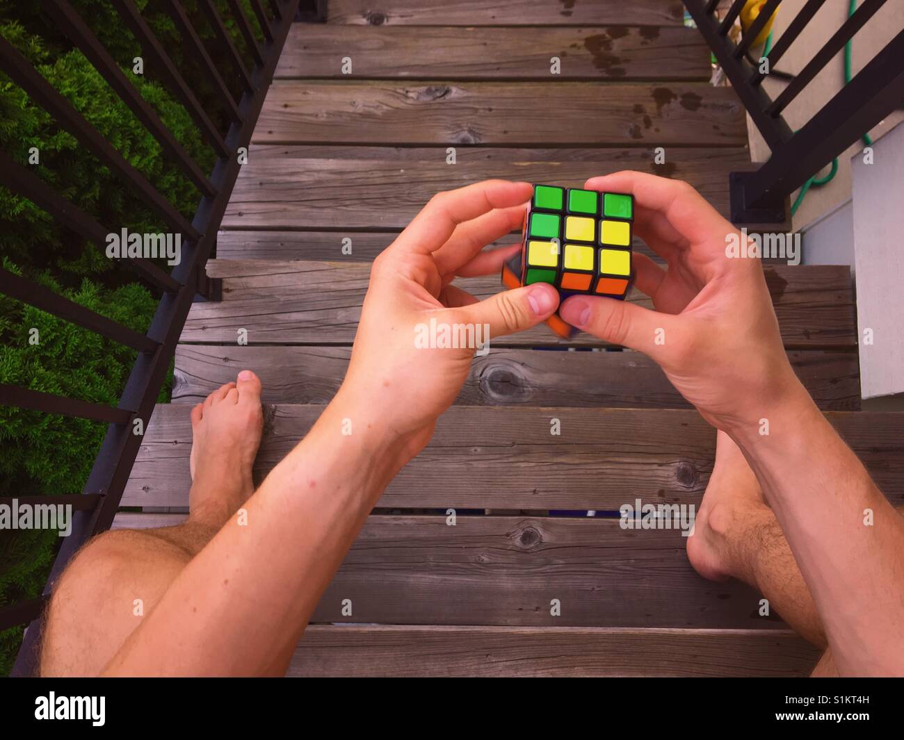 Young man solving Rubik's cube while sitting atop wooden stairs. - Smartphone Captured Stock Image