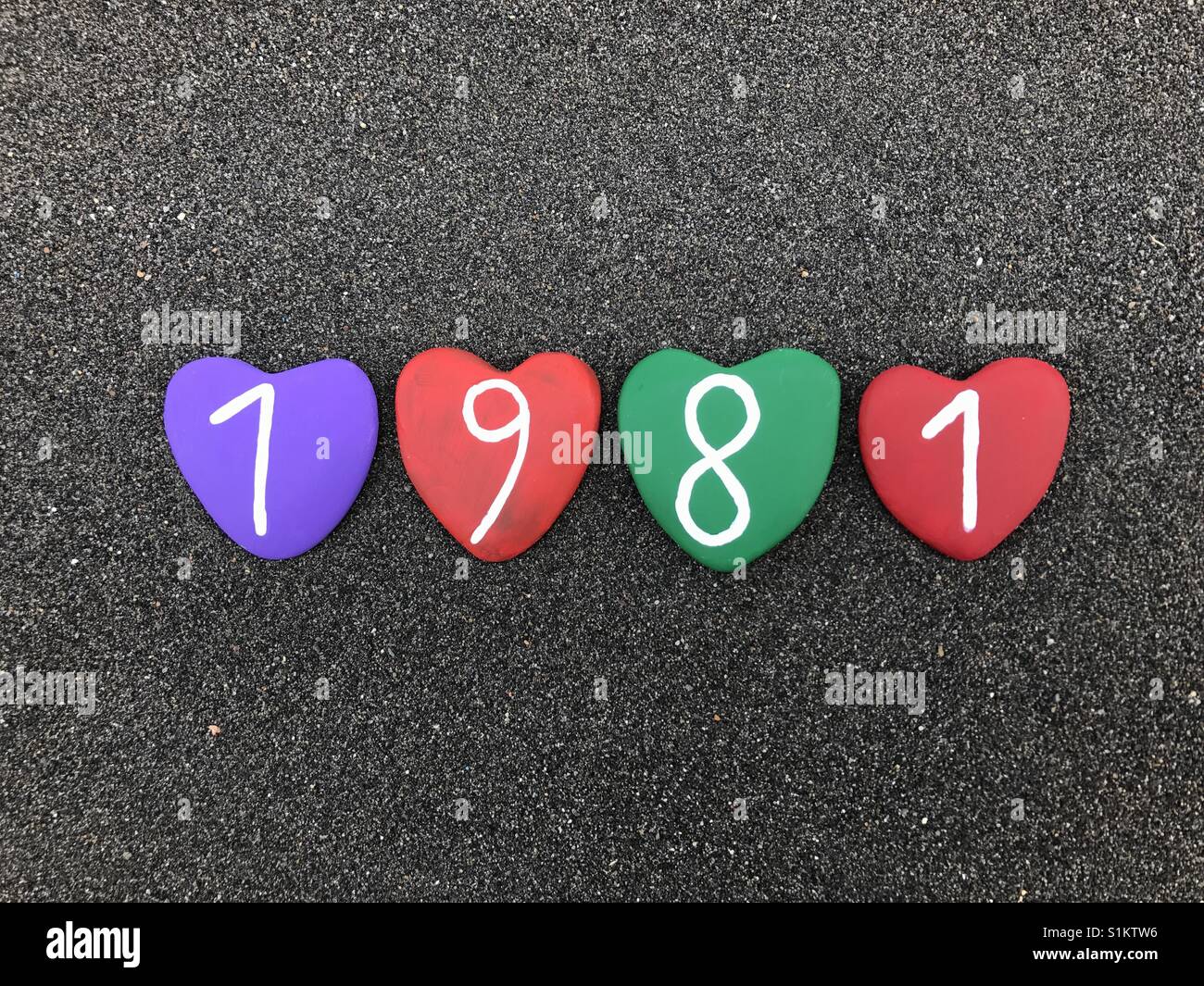 1981 year with colored heart stones over black volcanic sand Stock Photo