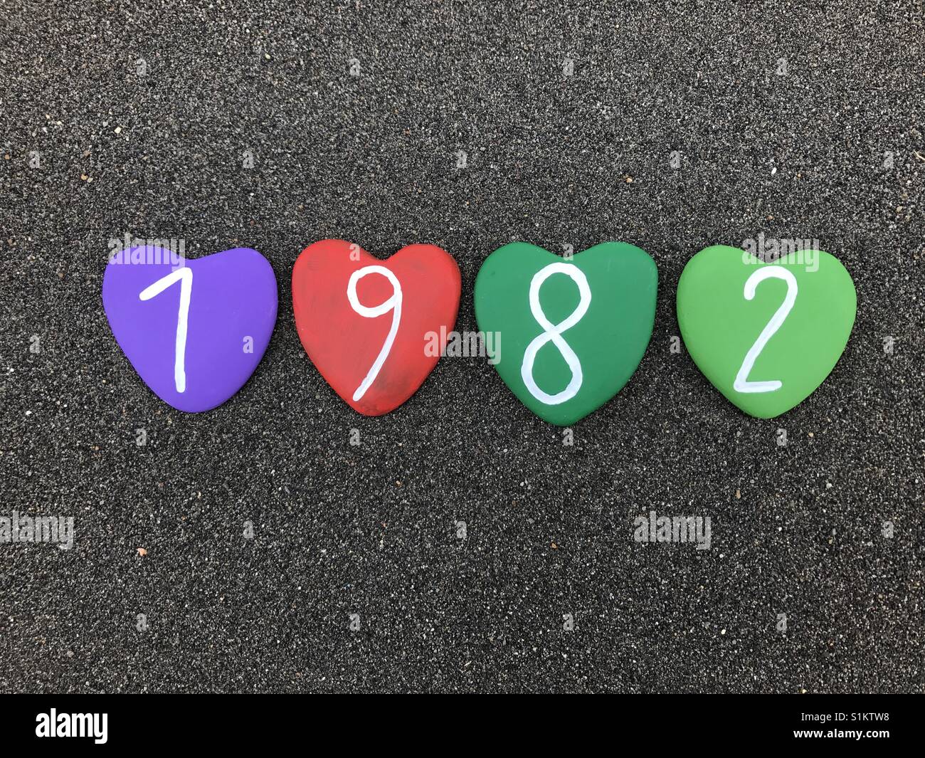 1982 year with colored heart stones over black volcanic sand - Smartphone Captured Stock Image