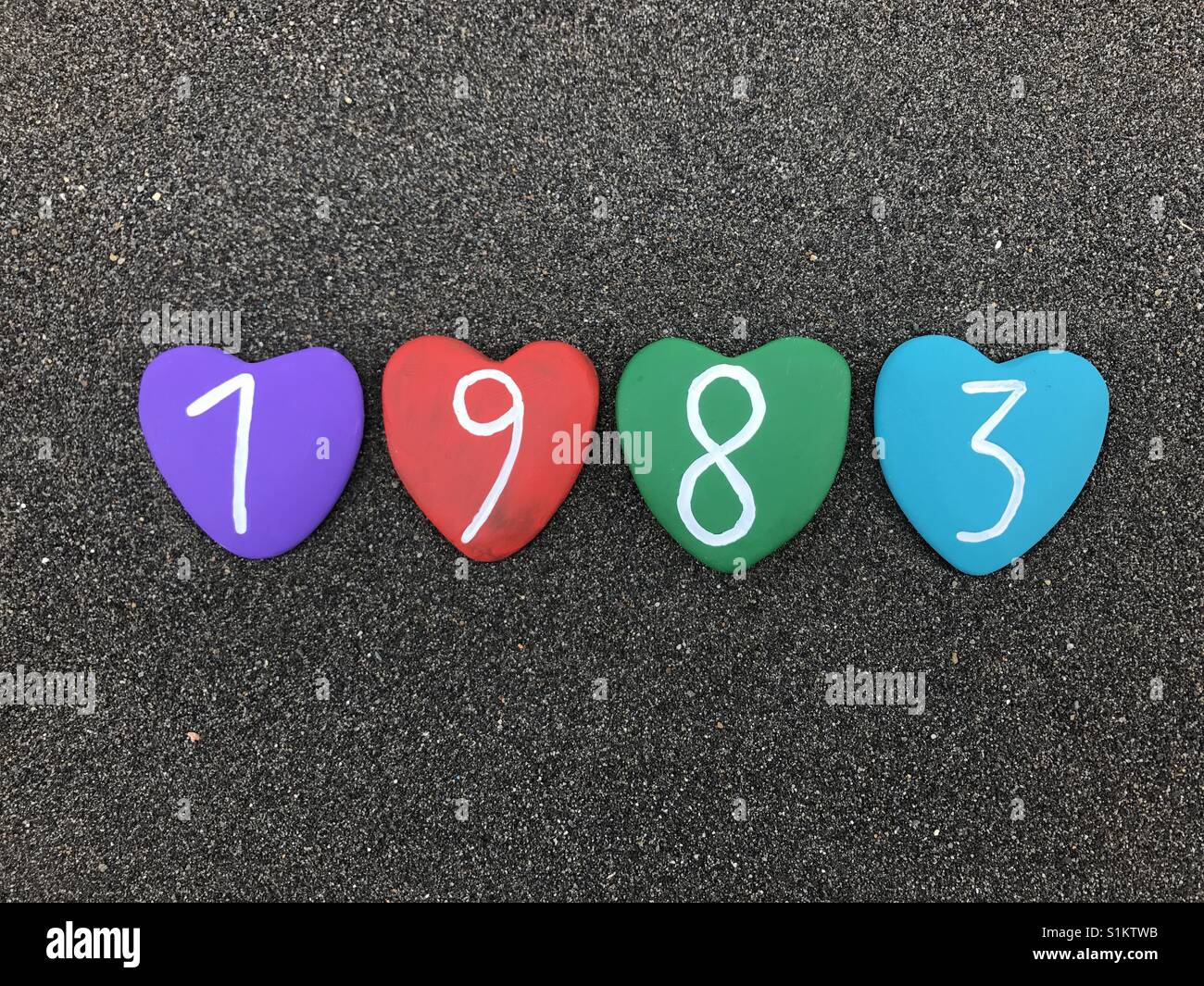 1983 year with colored heart stones over black volcanic sand Stock Photo