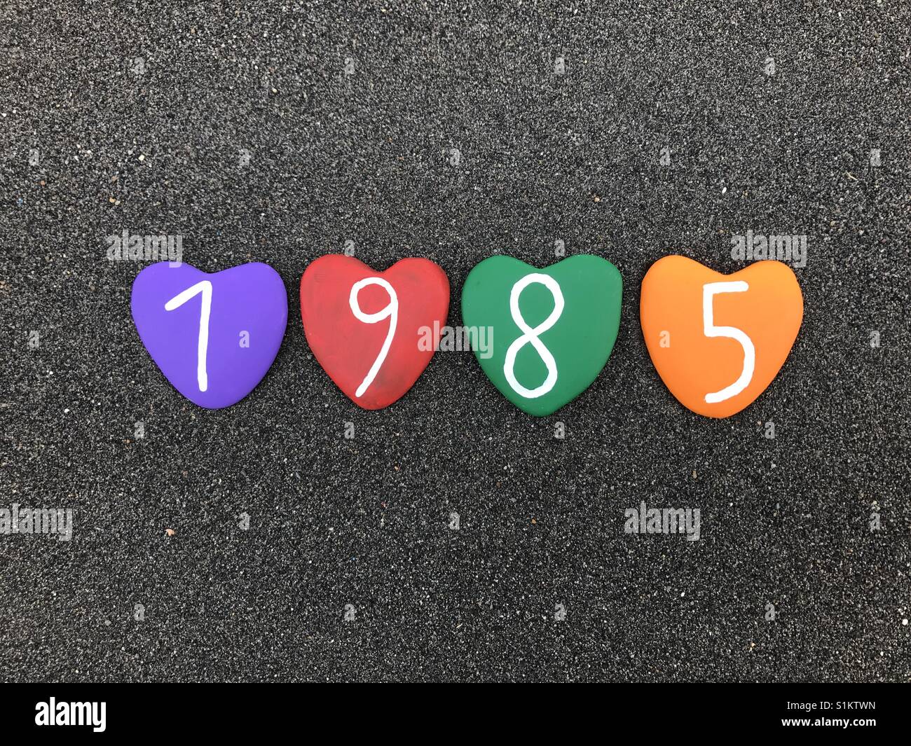 1985 year with colored heart stones over black volcanic sand - Smartphone Captured Stock Image