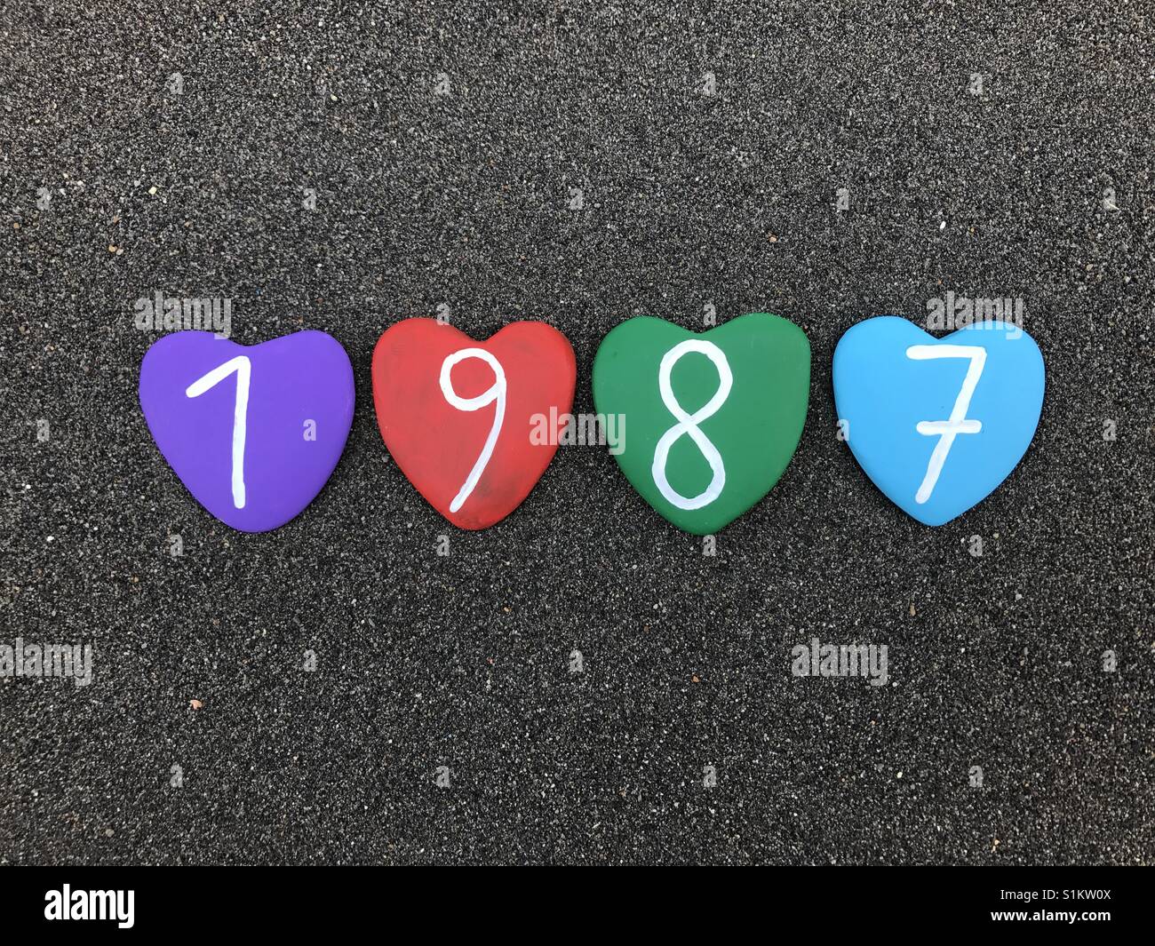 1988 year with colored heart stones over black volcanic sand - Smartphone Captured Stock Image