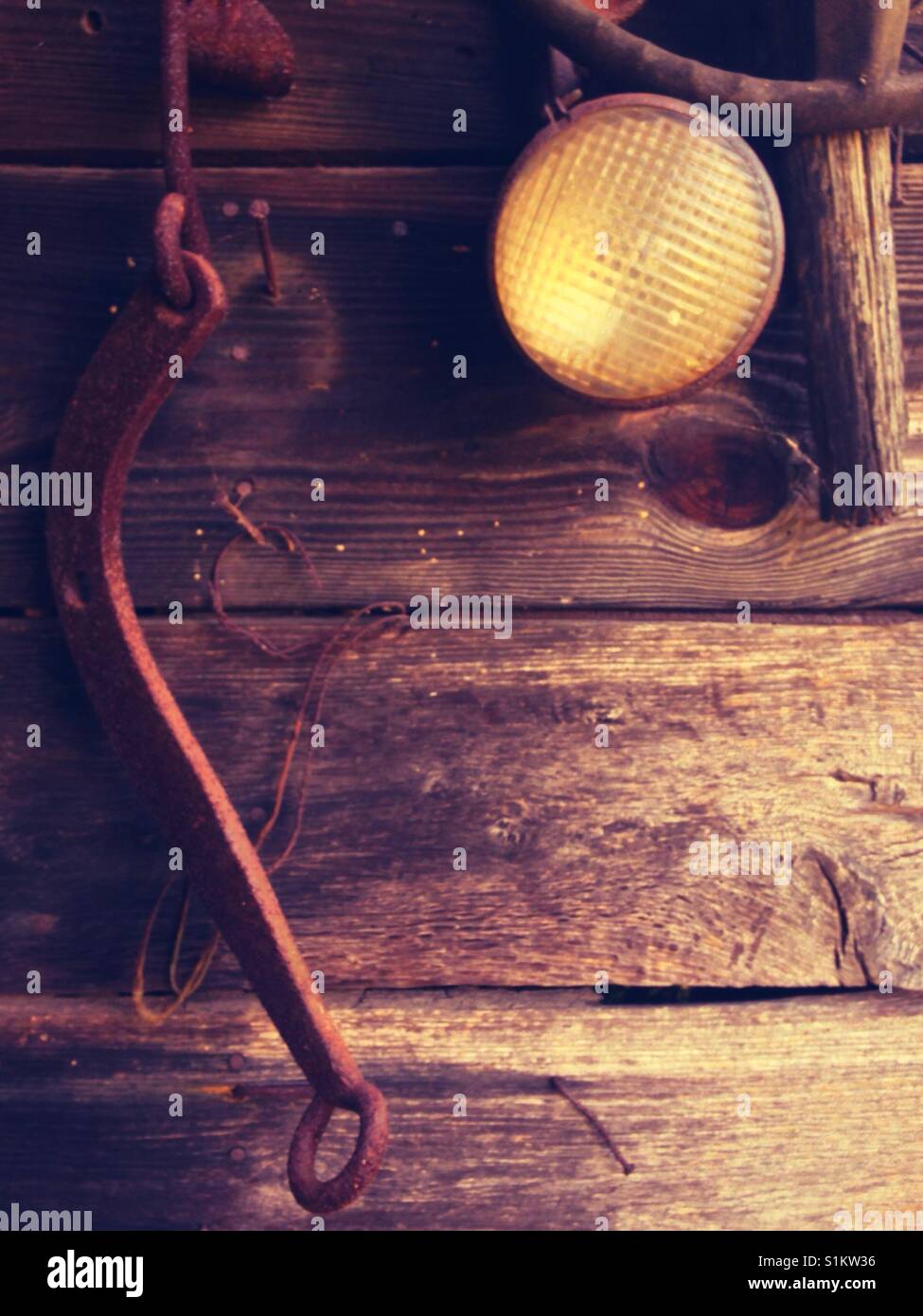 Headlight, steering wheel, and metal hardware hang on wooden wall of decrepit shed - Smartphone Captured Stock Image