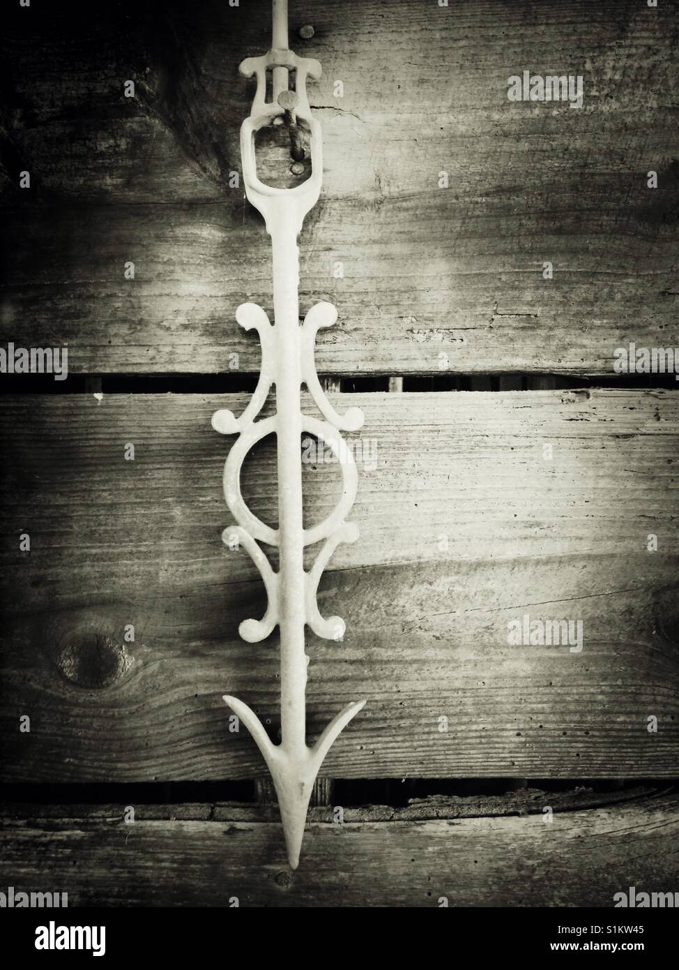 White cast iron weather vane arrow hangs pointing down in old wooden shed - Smartphone Captured Stock Image