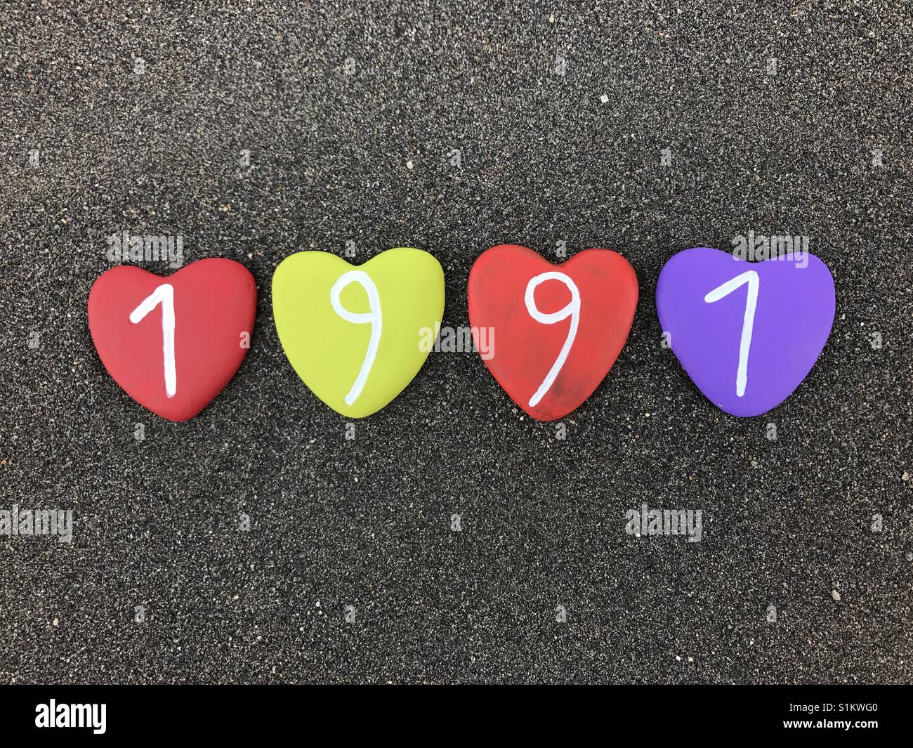 1991 year with colored heart stones over black volcanic sand - Smartphone Captured Stock Image