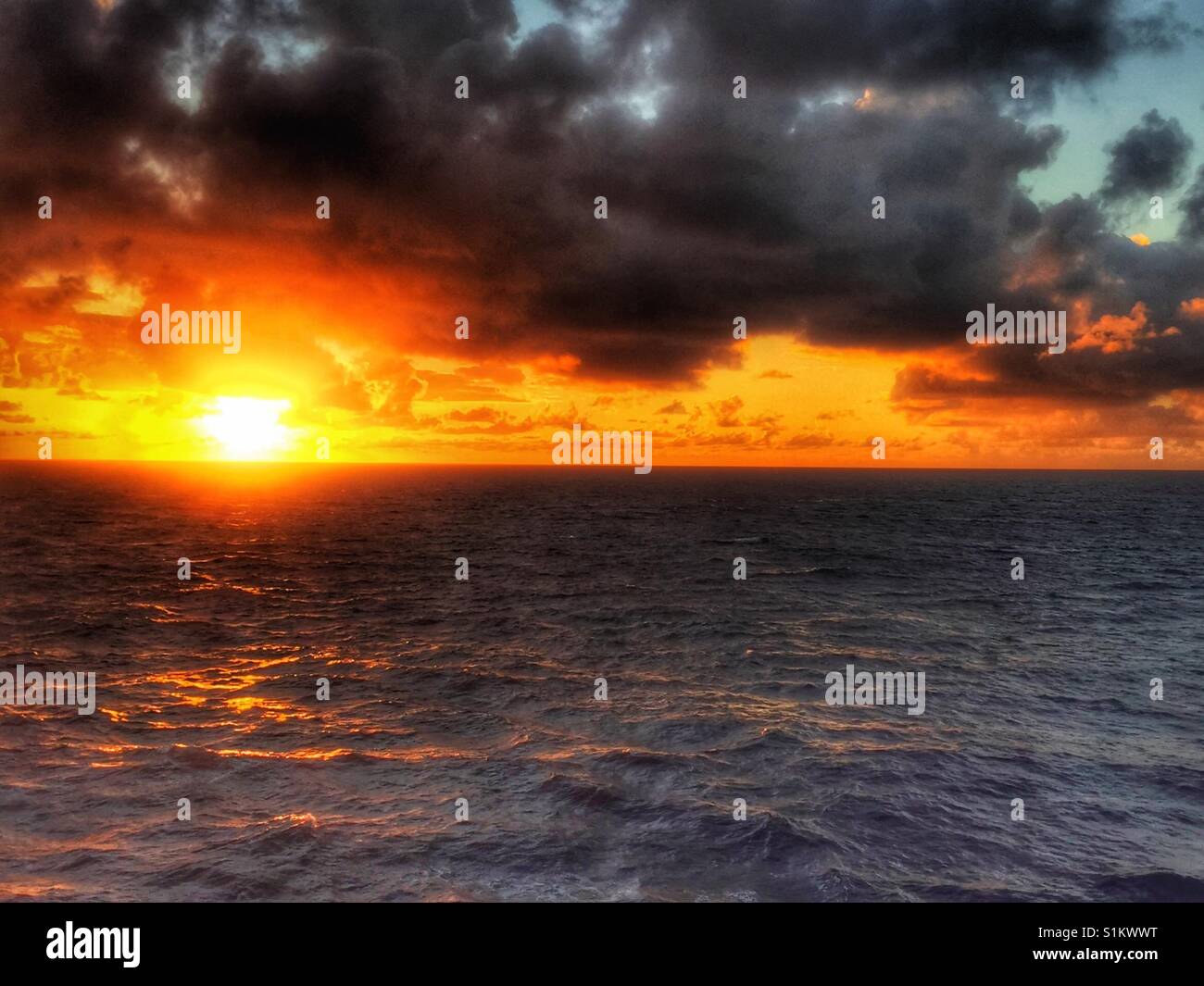 Sun peeks up over the Pacific Ocean for stunning sunrise on a cloudy day. Moody sunrise seascape. Ocean lit by rising sun on horizon. Stock Photo