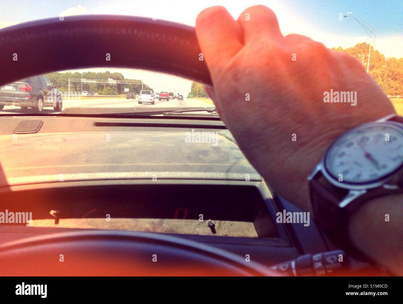 Making time on the interstate- photo of hand with watch on steering wheel with view of interstate traffic out windshield - Smartphone Captured Stock Image