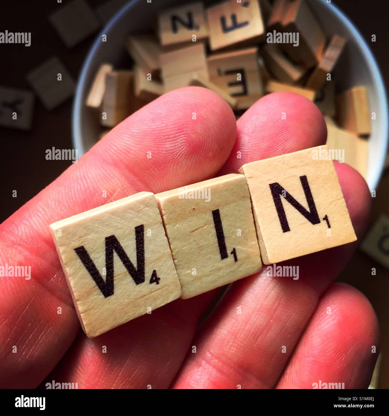 A close up shot of a man's hand holding wooden letters spelling win with other wooden letters in the background Stock Photo