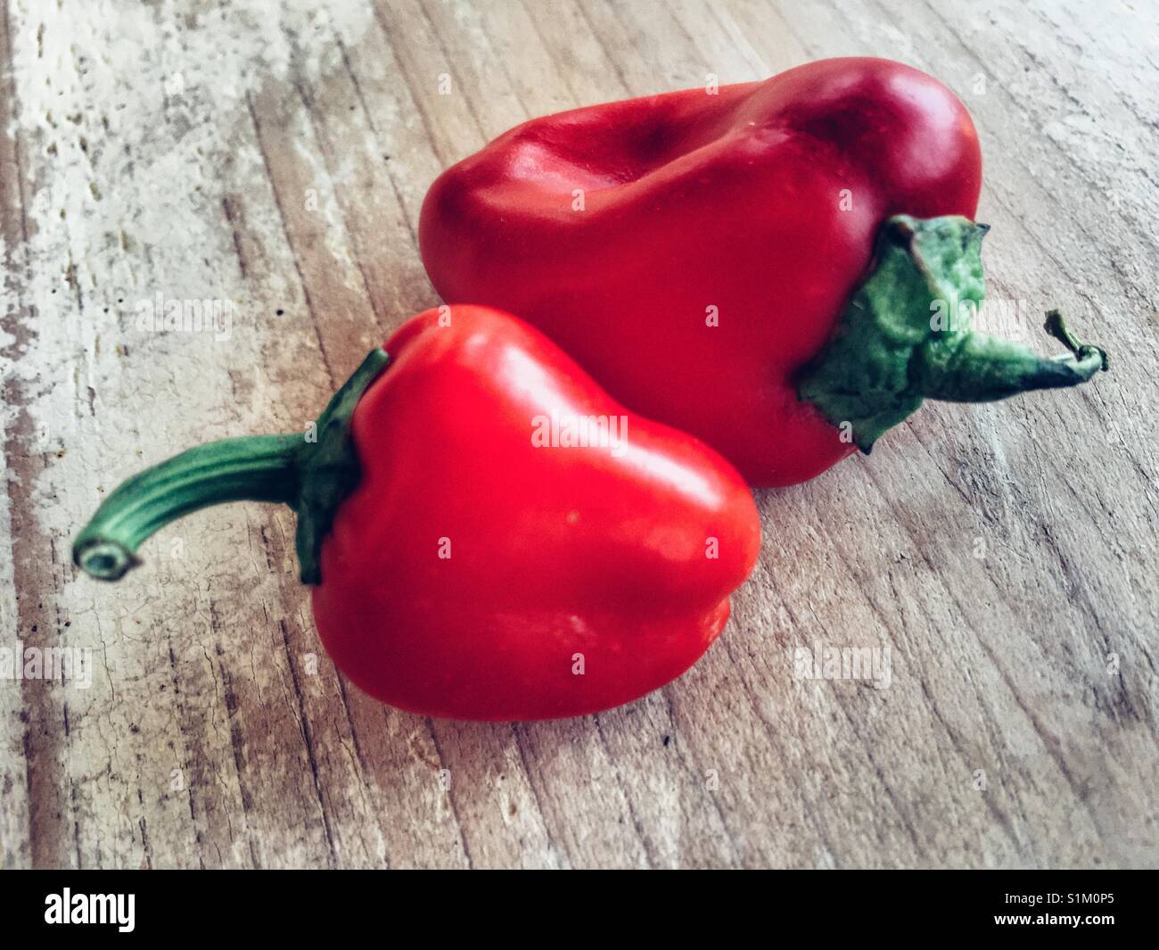 Two small red peppers on a wooden tabletop - Smartphone Captured Stock Image