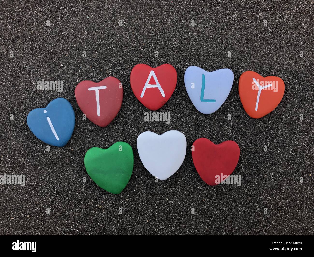 Italy, country name with colored heart stones over black volcanic sand - Smartphone Captured Stock Image