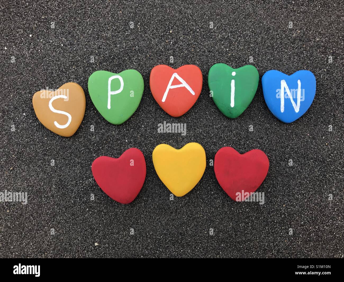 Spain with colored heart stones over black volcanic sand - Smartphone Captured Stock Image