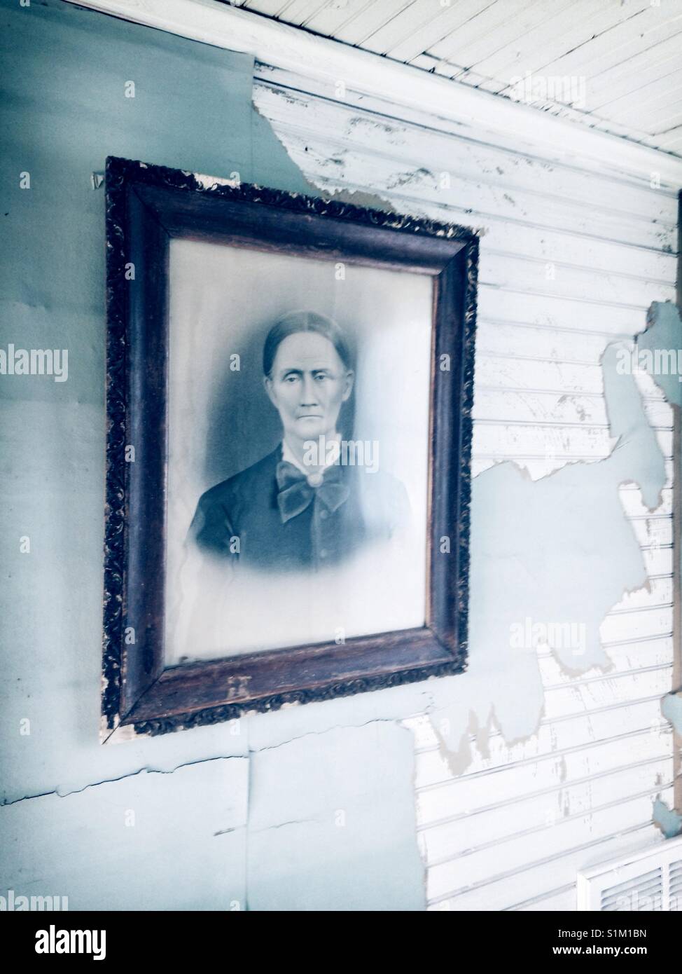 Portrait of stern Victorian woman in wooden frame hangs on wall with torn green wallpaper and white bead board- daguerreotype - Smartphone Captured Stock Image