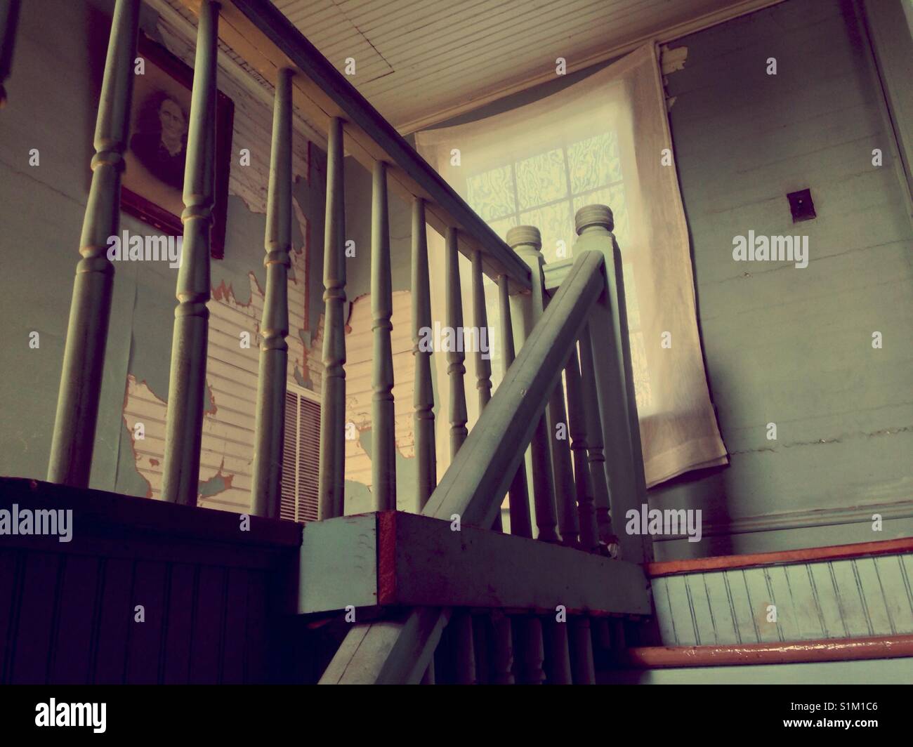 Victorian woman's portrait  on bead board and wallpapered wall as seen through stairway railing - Smartphone Captured Stock Image