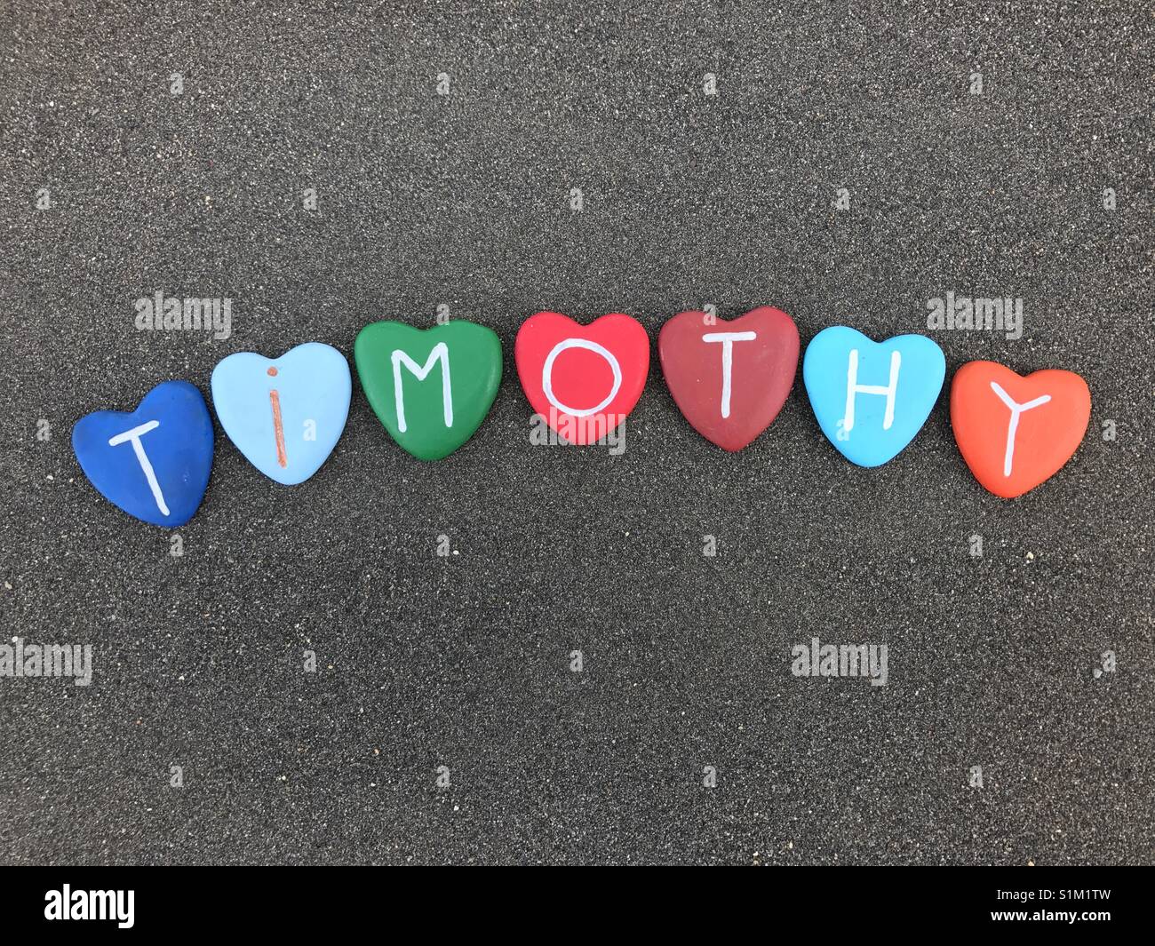 Timothy, masculine name with colored heart stones over black volcanic sand Stock Photo