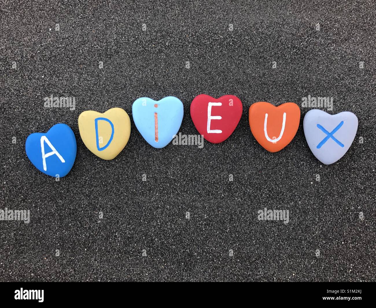 Adieux, french goodbye with multicolored heart stones over black volcanic sand Stock Photo