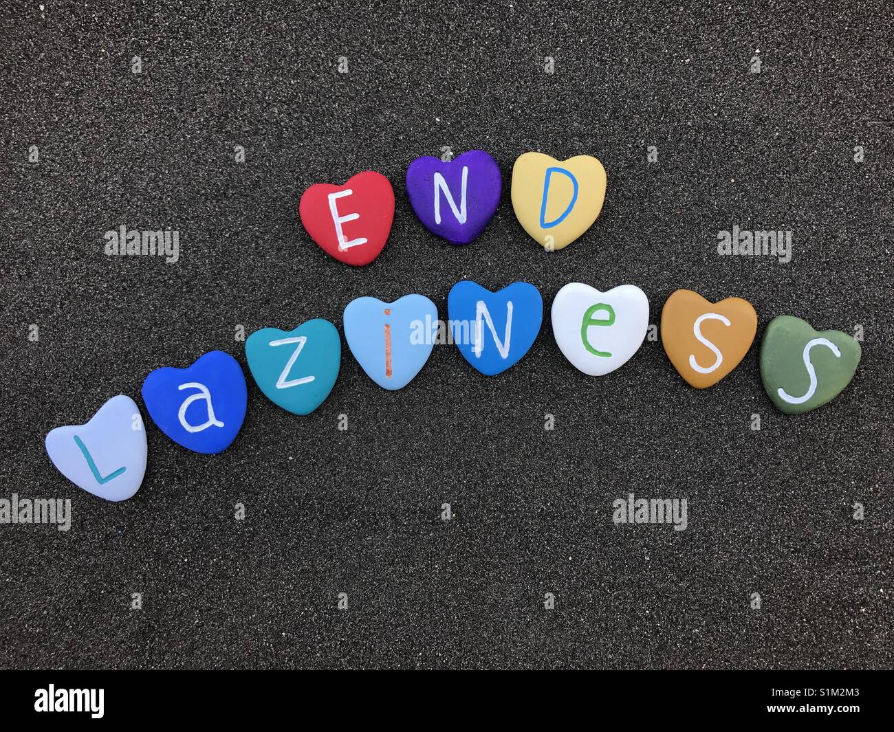 End laziness, motivational message with colored heart stones over black volcanic sand - Smartphone Captured Stock Image