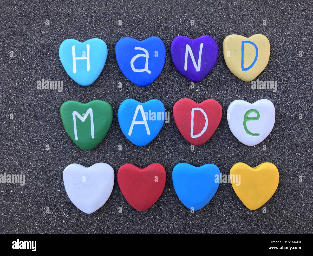 Handmade word with colored heart stones letters over black volcanic sand - Smartphone Captured Stock Image