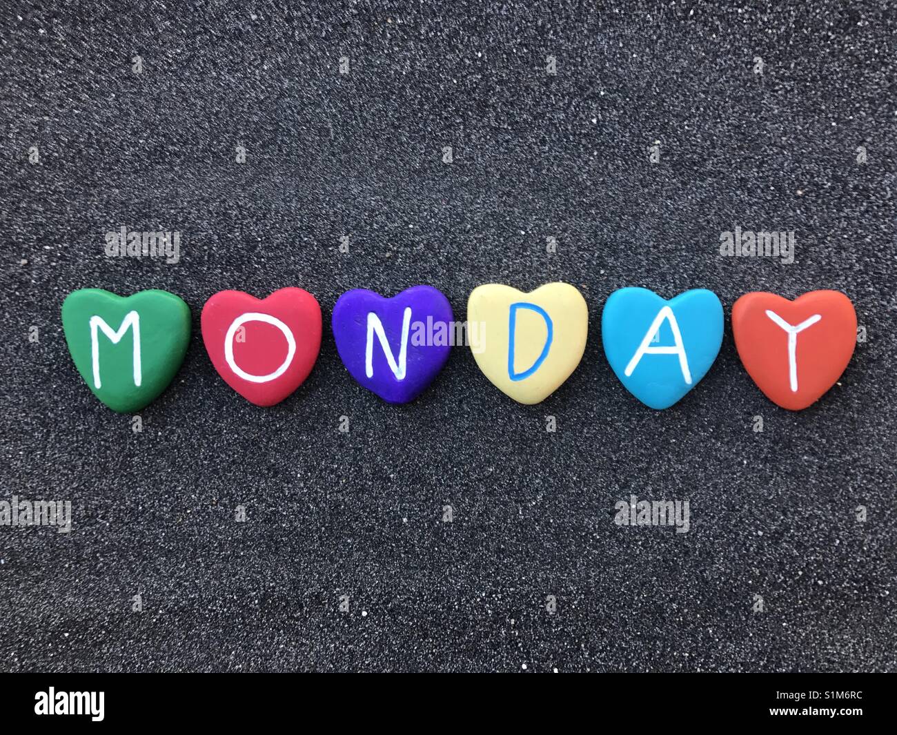 Monday, first day of the week with colored heart stones over black volcanic sand - Smartphone Captured Stock Image