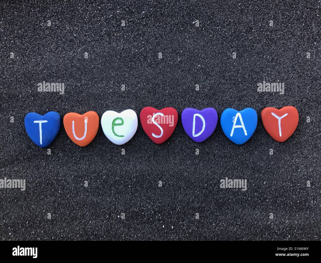 Tuesday, second day of the week with colored heart stones over black volcanic sand - Smartphone Captured Stock Image