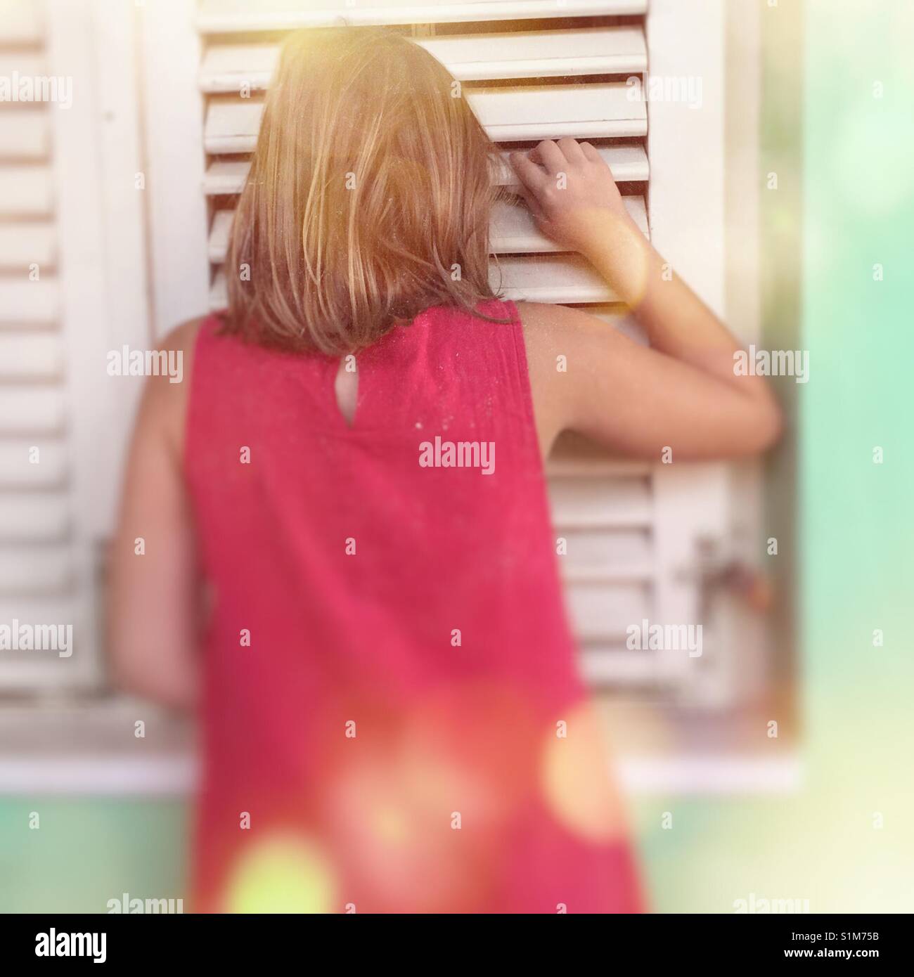 Curious little girl looking through window blinds Stock Photo